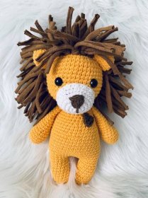 a crocheted lion stuffed animal laying on top of a white fur covered floor