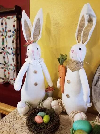 two stuffed rabbits sitting on top of a table next to some eggs and carrots