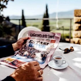 Eine Nahaufnahme eines Lesers der La Gazzetta auf einer italienischen Terrasse mit einer Espressotasse der Kaffeerösterei Martermühle