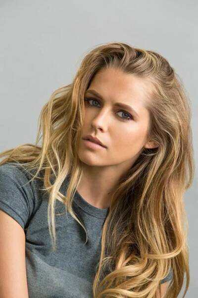 a beautiful blonde woman with long hair posing for a photo in front of a gray background