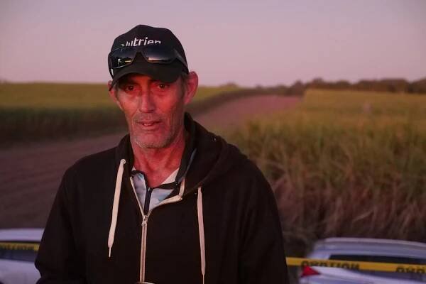 Sugarcane Farmer Bill Holding stands in front of a green sugarcane field at dusk. 