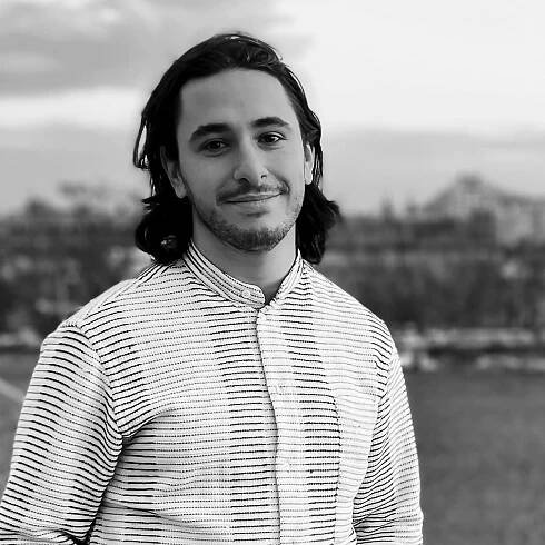 Photo of Antonio Starnino with white button up shirt with black horizontal lines with a cityscape backdrop
