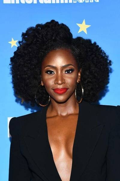 Teyonah Parris wears a twist out with big hoops, a low-cut black blazer, and red lipstick