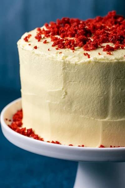 Frosted and decorated vegan red velvet cake on a white cake stand.