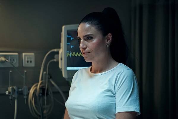 A woman nurse stands smiling conspiratorially in front of an EKG monitor