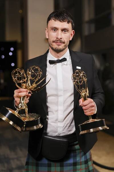 a man in a kilt is holding two emmy awards