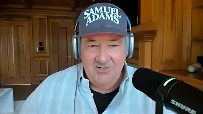 Brian Baumgartner wearing a Samuel Adams hat and headphones during an interview.