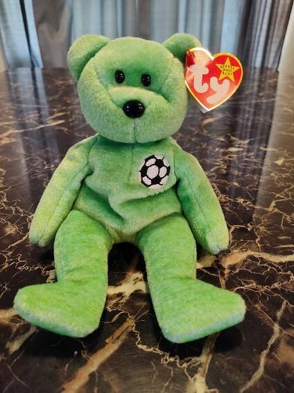 a green teddy bear sitting on top of a marble counter next to a red heart