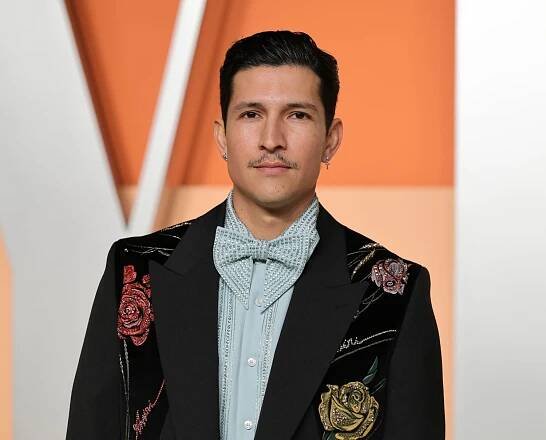 Danny Ramirez wearing a black embroidered blazer over a light blue button up and bow tie
