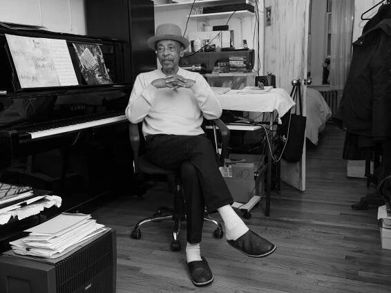 A black-and-white portrait shows Henry Threadgill, in a hat, seated at an upright piano in a wheeled office chair.
