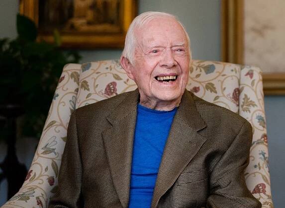 Jimmy Carter, smiling and sitting in a chair.