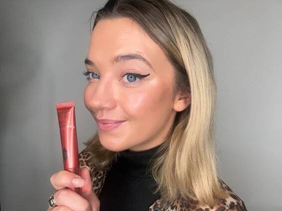 a woman in a leopard print shirt is holding a tube of charlotte tilbury makeup