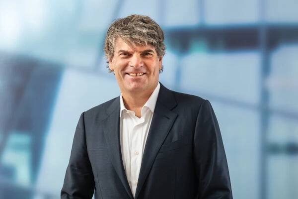 Auf dem Bild ist Oliver Wolff, Hauptgeschäftsführer des Verbandes Deutscher Verkehrsunternehmen (VDV), abgebildet. Er trägt ein dunkelblaues Sakko und ein weißes Hemd und lächelt in die Kamera. Der Hintergrund ist verschwommen.