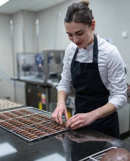 A pastry chef arranging chocolate eggs on a cooling rack.
