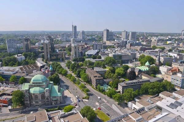 Aerial view of a modern city with green spaces, buildings, and a notable domed structure with green roofing.