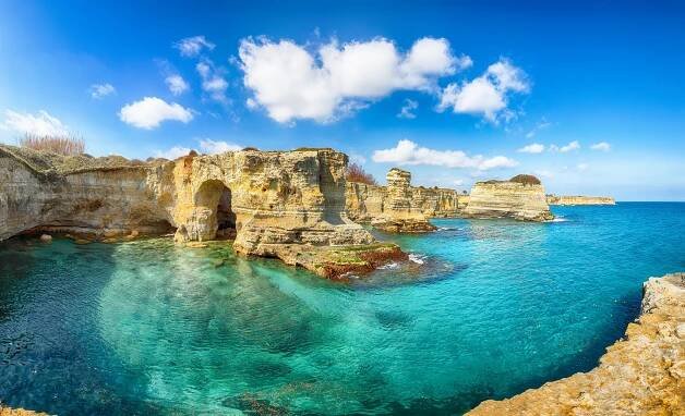 Ohromující mořská scenérie s útesy, skalnatým obloukem a stohy (faraglioni) v Torre Sant Andrea stock fotka