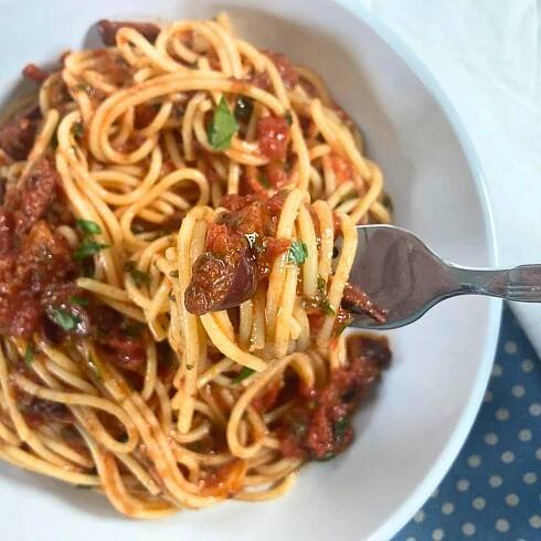 Spaghetti alla puttanesca on a fork lifting from a white plate.