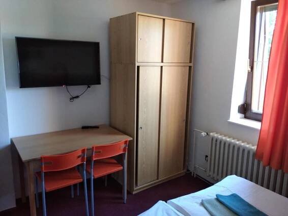a bedroom with a desk and a cabinet with a television at Penzion Beta in Luhačovice