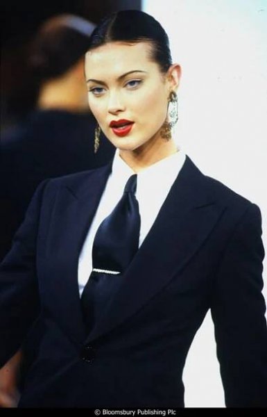 a woman in a black suit and white shirt with red lipstick on her lips is looking off to the side