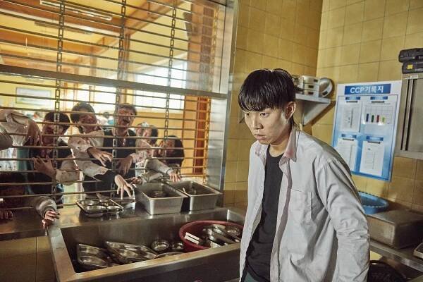 Yoo In-soo as Yoon Gwi-nam looking scared in a kitchen with zombies on the other side of the wall in All of us are Dead