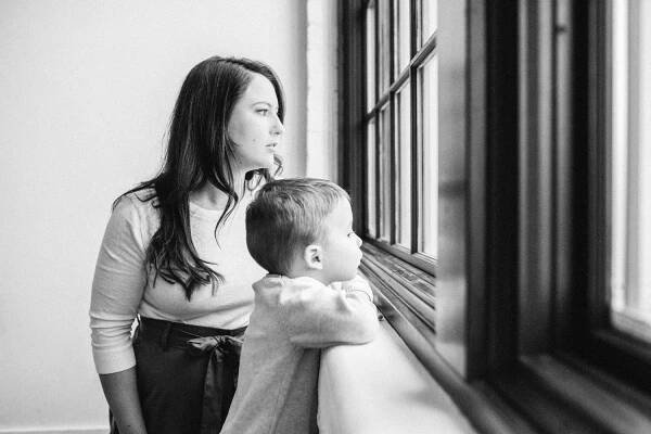 Parent and child looking out window together in black and white indoor portrait.