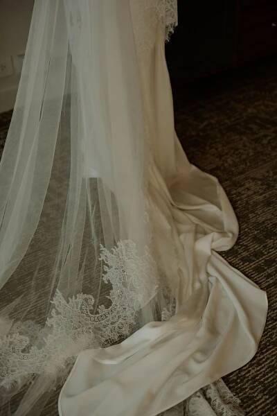 Elegant white wedding dress train with delicate lace detail and flowing veil on carpet.