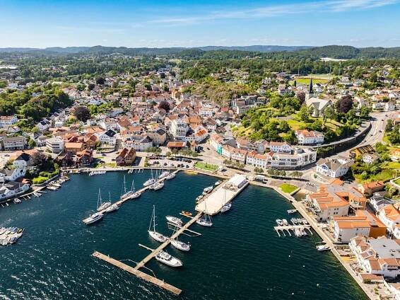 Aerial view of a coastal town with boats docked at piers, surrounded by dense buildings and green hills.