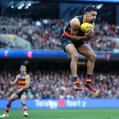An Adelaide Crows player jumps in the air with his knees and legs drawn up as he takes a mark.