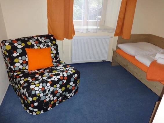 a room with a bed and a chair with an orange pillow at Hotel Praha Potštejn in Potštejn