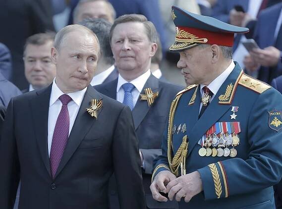 Vladimir Putin a ruský ministr obrany Sergej Šojgu. Uprostřed v pozadí šéf...