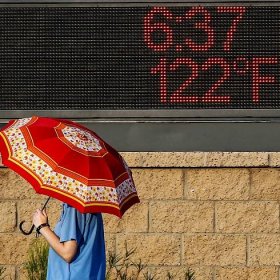 A pedestrian uses an umbrella to get some relief from the sun as she walks past a sign displaying the temperature on June 20, 2017 in Phoenix, Arizona.