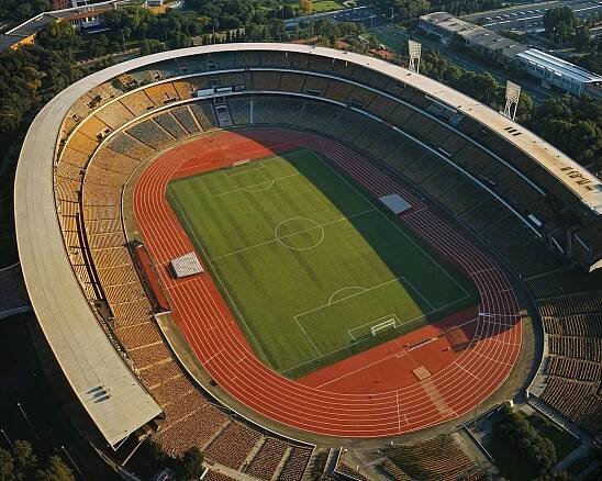 A birds-eye view of a grand stadium, showcasing the vast expanse of a sports field encircled by tracks, inspiring visions of athletic excellence and community spirit.