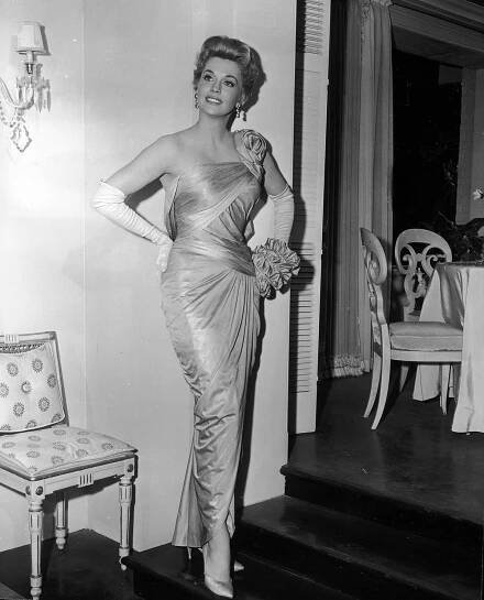 1960:  Full-length portrait of American actor Donna Douglas posing in a formfitting, draped, silk gown, designed by Walter Plunkett
