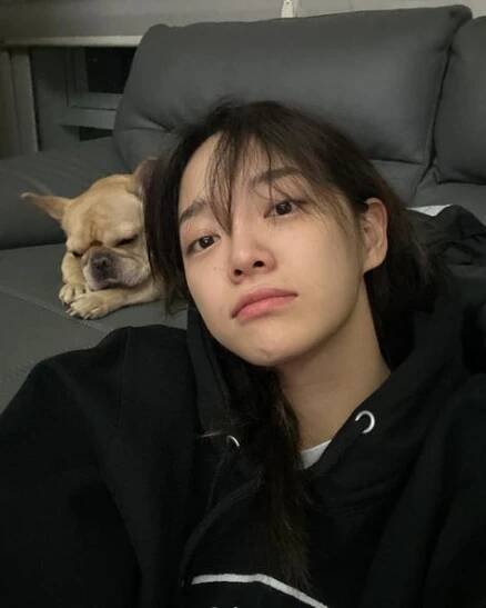 a woman laying on top of a couch next to a dog sleeping in the background