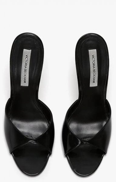 A pair of black, open-toe, slip-on women’s shoes with a crisscross design and seductive curved heel, insoles labeled "Classic Mule In Black Calf Leather by Victoria Beckham.