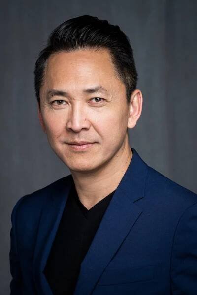 A photograph of the author Viet Thanh Nguyen, who is wearing a dark blue suit jacket and a black shirt.