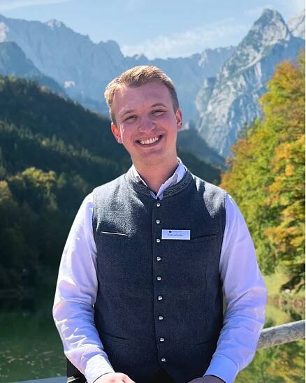 Portraitfoto vom Management Assistent Franz Ostler. Im Hintergrund sind die Berge und der Riessersee zu sehen.