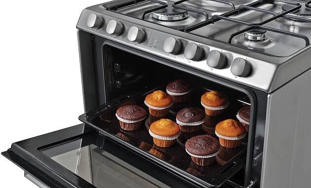 Nerezový sporák s otevřenými dvířky trouby a muffiny na plechu