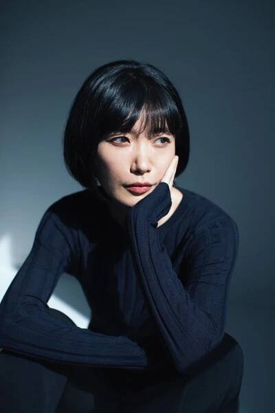 A portrait of Mieko Kawakami. She rests her head in her hand.