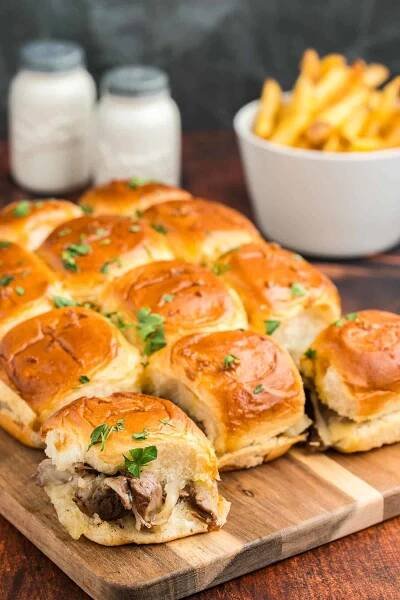 Philly cheesesteak sliders on a wooden cutting board.