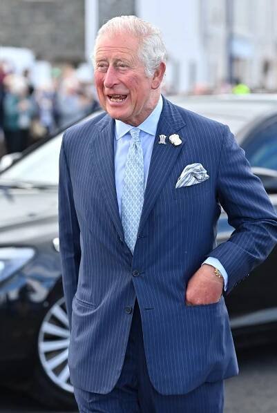 an older man in a suit and tie walking down the street with his hand on his hip