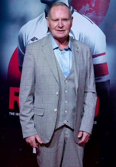 a man in a suit stands in front of a poster that says " the instinct "