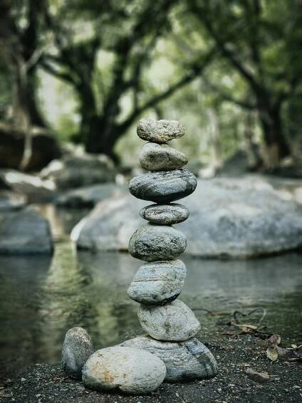Free A serene stack of stones balanced beside a peaceful stream in a wooded environment. Stock Photo
