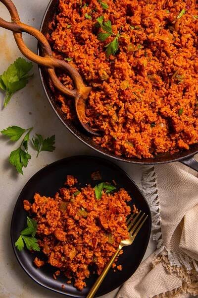 baked Gullah Red Rice in large black pan with wooden utensil on the side and small black plate with gold fork