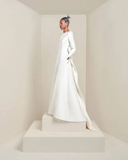 Model facing side wearing long sleeve a-line gown with button detail down the sleeves and pockets