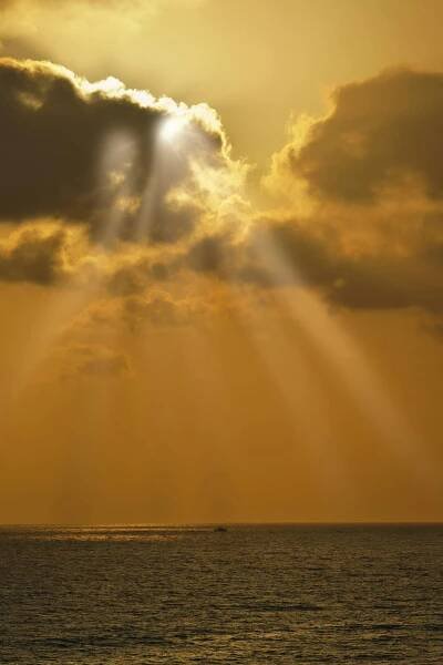 Free Sun rays piercing through clouds over a golden-hued sea, creating a dramatic and serene seascape. Stock Photo