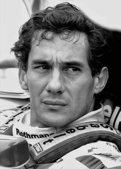 a black and white photo of a man sitting in a car wearing a racing suit