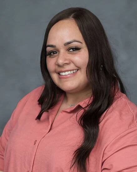 Professional headshot in coral-colored blouse against studio grey background.