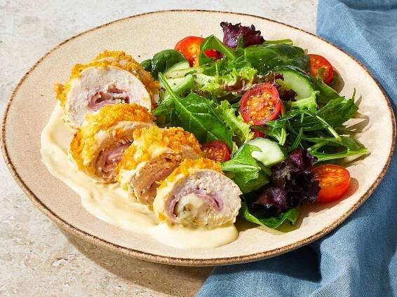 a sliced cordon bleu chicken roll served on a plate, with cordon bleu sauce on the side and a side of mixed greens salad.
