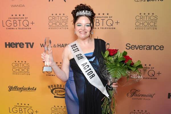 Person in elegant gown and tiara holds a trophy and roses at an LGBTQ+ Cinema &amp; TV event. Sash reads "Best Gay Actor."